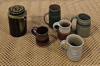 Photo of the coffee pot and 6 uniquely glazed ceramic mugs on woven mat