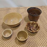 Five ceramic items on woven mat: large brown planter, large cream bowl, two small cream bowls with blue rims, sponge ware bowl