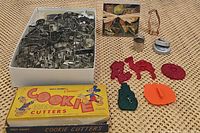 Wide view showing large quantity of metal cookie cutters in a box, vintage Disney cookie cutters box, Halloween box, and colorful plastic cutters laid out on surface.