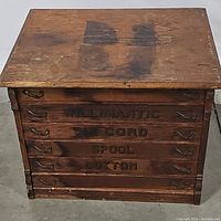 Front view of antique walnut spool cabinet showing six drawers with stenciled labels and metal handles.