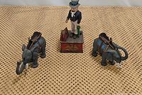 Photo of the three mechanical coin banks showing a pair of elephants and an Uncle Sam figure on a red base.