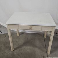 Front view of the white metal top desk showing its single drawer and four legs.