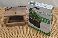 Photo of AeroGarden box and wooden bird feeder on table, showing overall items in lot.
