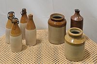 Lot of antique pottery and ceramic bottles including 4 ceramic beer bottles, stoneware crocks and antique pottery jars on a textured surface