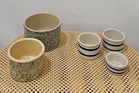 All 5 pottery bowls arranged on woven mat: 3 blue-striped, 2 blue spongeware pattern bowls.