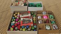 Wide shot showing four boxes containing various vintage Christmas bulbs and wax figurine candles arranged on carpeted floor.
