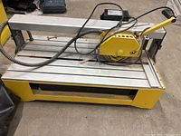 Front angled view of the yellow and silver 24-inch QEP bridge saw wet tile cutter showing motor and cutting arm on tiled floor.