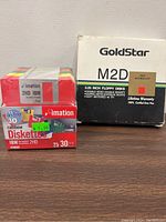 Photo showing a box of GoldStar M2D 5.25 inch floppy disks and a box of Imation 2HD IBM rainbow-colored 3.5 inch floppy diskettes with quantity and capacity details