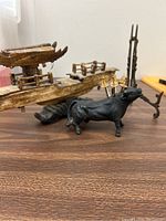 Wooden carved ship and black brass bull with gold cocktail swords, brown wood grain surface