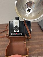 Front view of Brownie Hawkeye Flash Model camera in open brown leather carrying case showing camera face and flash attachment.