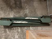 Green painted metal beams and brackets lying on a concrete floor, showing wear and rust marks.