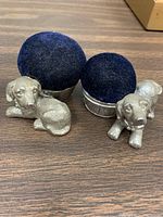 Two silver-tone dog figures attached to round blue velvet pin cushions.