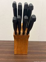 Wooden knife block holding 8 knives with black handles seen from above.