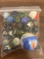 Front view of the resealable bag containing about 30 mixed vintage glass marbles, showing many colorful, swirled patterns and large white marble with blue and orange swirls.