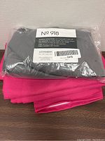 Photo showing two window curtains; one grey curtain sealed in plastic packaging labeled No 918 Lichtenberg and one bright pink curtain unfolded beneath it.