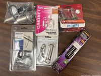 Photo showing a variety of home hardware items including cabinet lock, shower curtain hooks, drawer hardware, hinge glide, and a Philips light bulb.