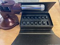 Ring stretcher machine with adjustable rod and base, alongside a black case holding 11 black die molds.