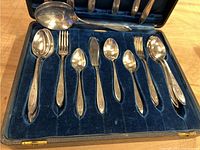 View of the silver plated flatware arranged in a blue velvet lined case showing spoons, forks, knives and serving utensils.