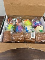 Opened box contains multiple squishy toys individually wrapped in plastic. There are colorful dinosaur shaped toys, a squirrel character squishy, and brown tree trunk squishy bases.