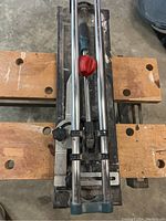 Top view of the manual tile cutter showing the red adjustment knob and chrome rails mounted on a workbench