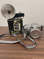 Silver Kodak camera with lens cap and strap next to Keystone electronic flash with original box