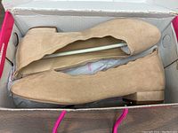 Top-down view of the nude suede flats inside original box, showing scalloped edge design and low heel.