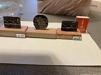 Three silver miniature wall sculptures on wood bases shown together with matchbox for scale