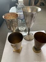 Four Kiddush caps positioned next to a water bottle for size reference displayed on a white surface.