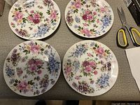 Four decorative plates showing detailed floral pattern with pink, blue, purple flowers on white background.