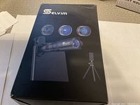 Box front showing product name 'Selvim' and images of the four lenses, mount clip and tripod included in the kit.