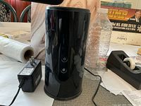 Black cylindrical D-Link DIR-860L wireless router with power adapter, shown on table with other items in background.