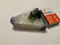 Jade elephant figurine holding a leaf displayed on an amethyst crystal base from a side angle with match box for scale.