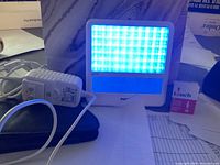 Philips GoLite blue light device powered on showing bright blue LED lights, with included white charger and black carrying case.