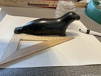 Solid dark stone sculpture of a seal about 9 inches long shown from side with ruler for scale.