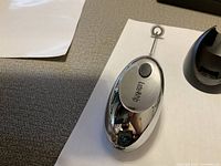 Handheld chrome electric milk frother laying on paper, showing its front side with button and Latte-Whip branding.