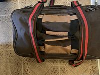 Top view of the brown and tan travel bag showing the padded handles and shoulder strap with red and black stripes.