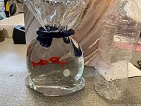 Clear Murano glass figurine shaped like a fish bowl with two red fish inside and blue glass accents at the neck.