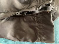 Close-up of zipper pocket detail with brown stitching on muted tone fabric.