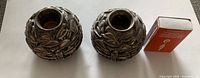 Pair of round silver candle holders shown from top angle with matchbox for scale