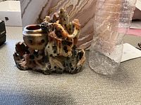 Front side view of the stone carving sculpture beside a water bottle for scale, showing bowl and textured elements.