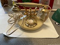 Front and side view of off-white and gold-tone vintage rotary phone with coiled cord and detailed handset.