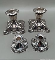 Two pairs of silver plated candlesticks shown together, highlighting size and design differences