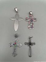 All four sterling silver cross pendants arranged on a grey surface, showing fronts and details.