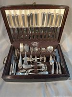 Open wooden case showing full flatware set with knives in lid and utensils in base