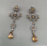 Full view of both chandelier earrings showing floral and heart motifs with gold and clear stones, teardrop peach pendants
