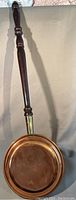 Full view of the copper bed warmer showing the long dark wooden handle attached to the copper pan with a brass connector.
