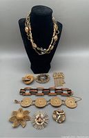 Photo of two necklaces displayed on a black bust with eight jewelry pieces laid out below including bracelets, brooches, hair barrette, scarf clip, and pendant
