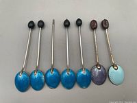 Seven vintage gilt sterling enamelled coffee spoons in various shades of blue and purple with coffee bean finials, one spoon missing finial.