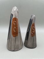 Two ceramic salt and pepper shakers photographed against a neutral background showing abstract black and brown patterns on a gray textured surface.