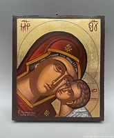 Full frontal image of the painted religious icon on wood panel showing Madonna and Child with gold background and red, white, and blue color scheme.